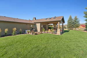 Rear view of house featuring a patio area, a lawn, a chimney, stucco siding, and roof with shingles
