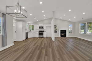 Unfurnished living room with dark wood finished floors, vaulted ceiling, a glass covered fireplace, a chandelier, and recessed lighting