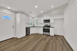 Kitchen featuring recessed lighting, white cabinets, vaulted ceiling, decorative backsplash, and stainless steel appliances