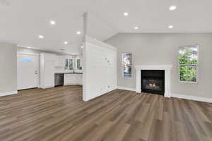 Unfurnished living room featuring recessed lighting, vaulted ceiling, dark wood-style flooring, and a glass covered fireplace