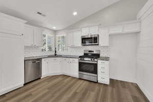 Kitchen featuring vaulted ceiling, recessed lighting, white cabinetry, appliances with stainless steel finishes, and backsplash