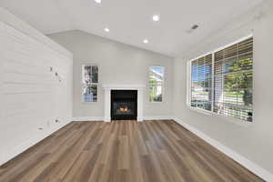 Unfurnished living room featuring lofted ceiling, a glass covered fireplace, wood finished floors, and recessed lighting