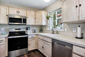 Kitchen featuring light brown cabinetry, stainless steel appliances, light countertops, and dark wood-style flooring