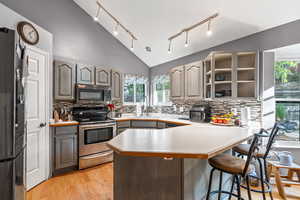 Kitchen with plenty of natural light, stainless steel appliances, light wood finished floors, a breakfast bar area, and high vaulted ceiling