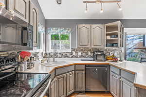 Kitchen featuring stainless steel appliances, backsplash, light countertops, vaulted ceiling, and gray cabinetry