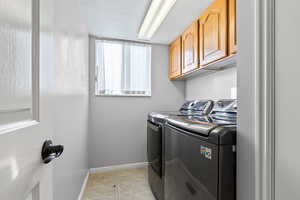 Laundry area with light tile patterned floors, cabinet space, and independent washer and dryer