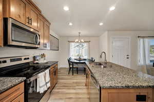 Kitchen with stainless steel appliances, light wood-style floors, dark stone countertops, recessed lighting, and brown cabinets
