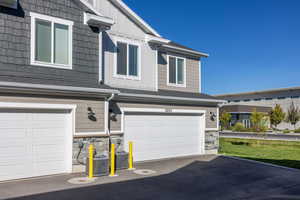 View of front facade with stone siding, board and batten siding, a shingled roof, and an attached garage