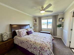 Bedroom featuring ornamental molding, a textured ceiling, dark carpet, and a ceiling fan
