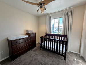 Bedroom with a nursery area, dark colored carpet, a textured ceiling, and ceiling fan