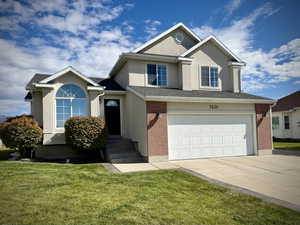 View of front of home with stucco siding, an attached garage, concrete driveway, a front lawn, and brick siding