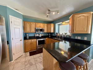 Kitchen featuring stainless steel appliances, a breakfast bar area, a textured ceiling, dark stone countertops, and light tile patterned floors