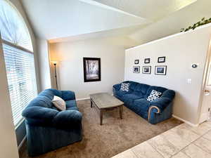 Carpeted living room with vaulted ceiling, a textured ceiling, and tile patterned flooring
