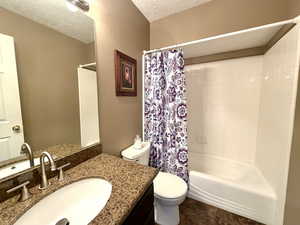 Full bathroom featuring shower / bath combo with shower curtain, vanity, and a textured ceiling
