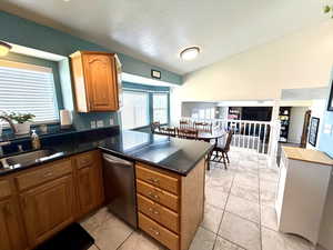 Kitchen with brown cabinetry, healthy amount of natural light, a textured ceiling, dishwasher, and vaulted ceiling