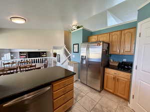 Kitchen with appliances with stainless steel finishes, a textured ceiling, dark stone countertops, brown cabinets, and vaulted ceiling