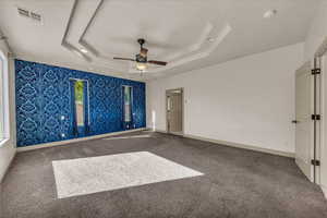 Carpeted empty room with a tray ceiling, wallpapered walls, and ceiling fan