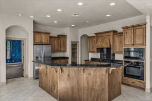 Kitchen featuring arched walkways, a kitchen bar, light tile patterned flooring, brown cabinetry, and recessed lighting