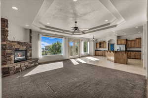 Unfurnished living room with a raised ceiling, a chandelier, a stone fireplace, light colored carpet, and recessed lighting