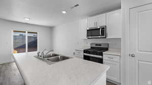 Kitchen with light countertops, appliances with stainless steel finishes, white cabinetry, wood finished floors, and recessed lighting