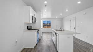 Kitchen with a kitchen island with sink, stainless steel appliances, light countertops, white cabinetry, and dark wood-style floors