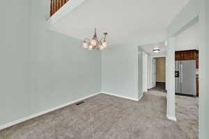 Empty room featuring light carpet and a chandelier