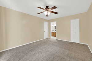Unfurnished bedroom featuring carpet flooring, ensuite bath, and ceiling fan