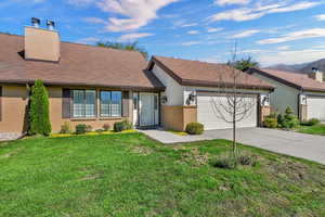 View of front of home with brick siding, concrete driveway, a front yard, an attached garage, and a chimney