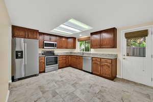 Kitchen featuring appliances with stainless steel finishes, brown cabinetry, and light stone countertops