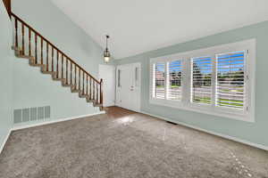 Entryway with carpet floors, stairway, and high vaulted ceiling