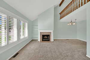 Unfurnished living room featuring carpet, a fireplace, high vaulted ceiling, built in shelves, and a chandelier