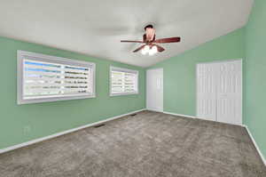 Unfurnished bedroom featuring multiple closets, carpet, vaulted ceiling, and a ceiling fan