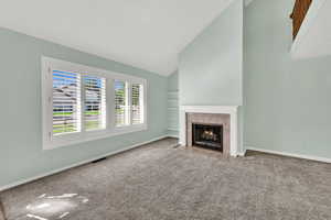 Unfurnished living room featuring carpet flooring, a tiled fireplace, high vaulted ceiling, and built in features