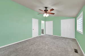 Unfurnished bedroom featuring vaulted ceiling, two closets, carpet, and ceiling fan