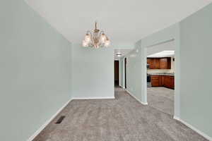 Unfurnished dining area featuring light carpet and a chandelier