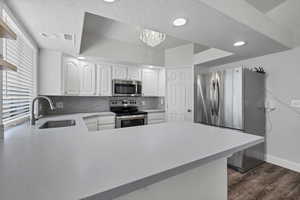 Kitchen with tasteful backsplash, appliances with stainless steel finishes, white cabinetry, light countertops, and a peninsula
