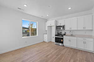 Kitchen featuring appliances with stainless steel finishes, white cabinetry, light wood finished floors, and recessed lighting