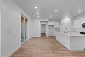 Kitchen with white cabinets, light wood-style flooring, recessed lighting, an island with sink, and stainless steel microwave