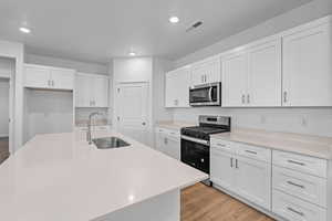 Kitchen featuring white cabinets, stainless steel appliances, recessed lighting, light wood-type flooring, and a center island with sink