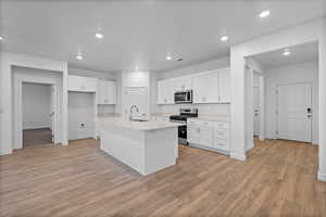 Kitchen featuring appliances with stainless steel finishes, white cabinetry, recessed lighting, an island with sink, and light wood-style floors