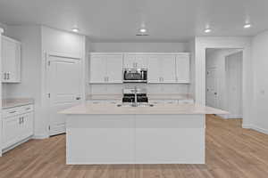 Kitchen with white cabinetry, stainless steel appliances, light wood-style flooring, recessed lighting, and a kitchen island with sink