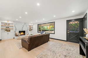 Living area with recessed lighting, a high end fireplace, built in shelves, and light wood-type flooring