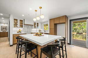 Kitchen with brown cabinets, a kitchen breakfast bar, pendant lighting, backsplash, and a center island
