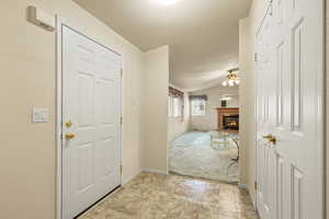 Foyer entrance featuring a glass covered fireplace, ceiling fan, light carpet, and vaulted ceiling