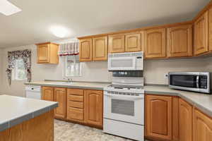 Kitchen featuring white appliances, tile countertops, and a skylight