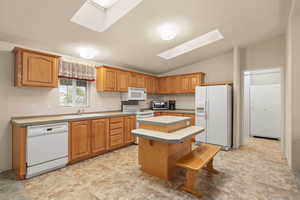 Kitchen with white appliances, vaulted ceiling, a center island, a skylight, and tile countertops