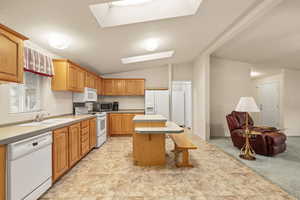 Kitchen featuring tile countertops, a kitchen island, a breakfast bar area, lofted ceiling, and white appliances