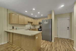 Kitchen featuring light brown cabinets, appliances with stainless steel finishes, light countertops, recessed lighting, and a peninsula