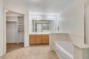 Bathroom featuring a shower stall, a spacious closet, a garden tub, double vanity, and a textured ceiling