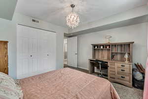 Bedroom with dark colored carpet, a chandelier, a closet, and an office area